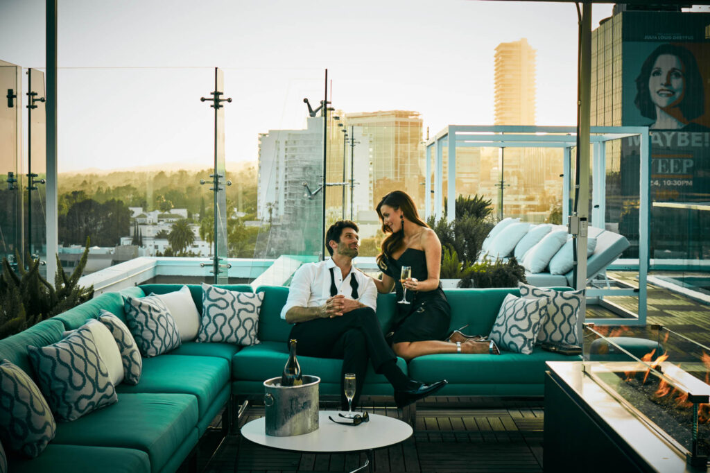 A couple sits on a teal sofa on the rooftop of The London Hotel in West Hollywood, California.