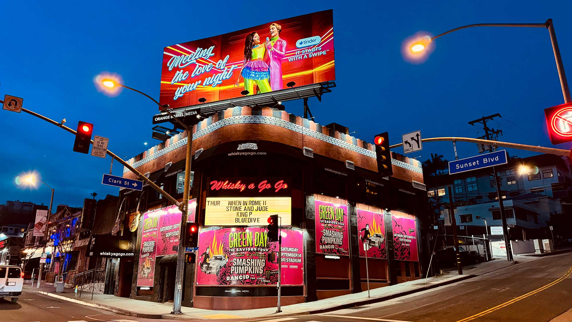 Exterior of the Whisky a Go Go nightclub at night, with pink promo posters covering the facade and a large colorful billboard above the building. West Hollywood, California.