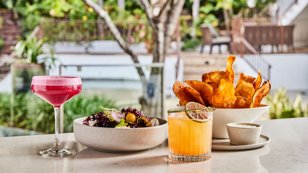 Multiple plates of food and a cocktail sit on an outdoor table at Cavatina in West Hollywood, California.